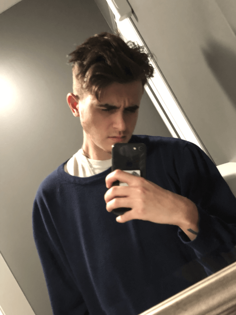 August wearing a navy sweater and taking a mirror selfie.