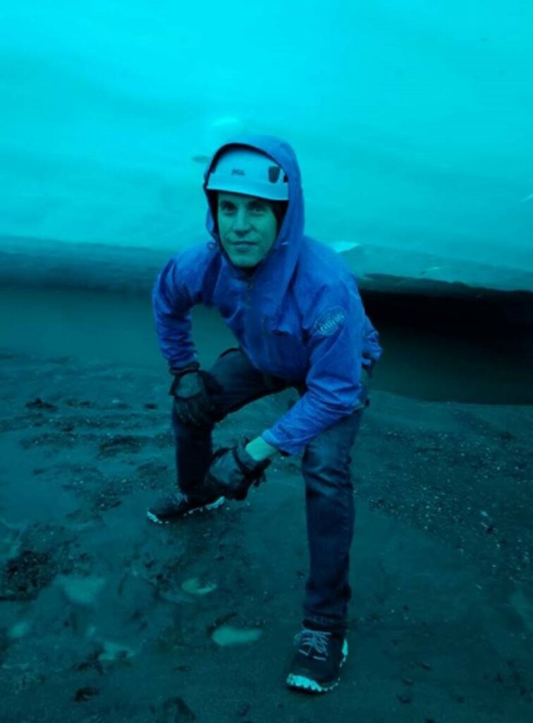 Clay crouched over underneath a bright blue glacier.